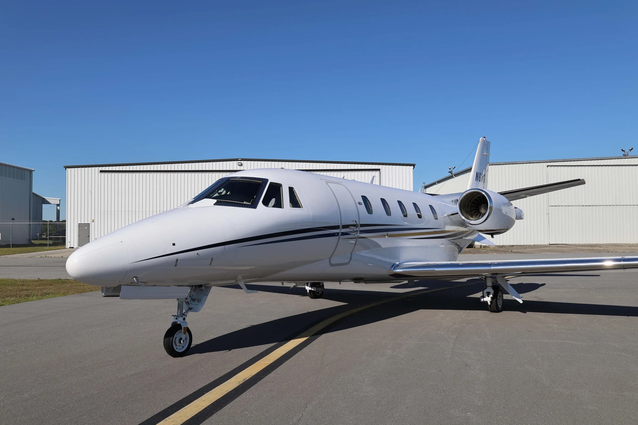 A white business jet with black and gold stripes parked on an airport tarmac.