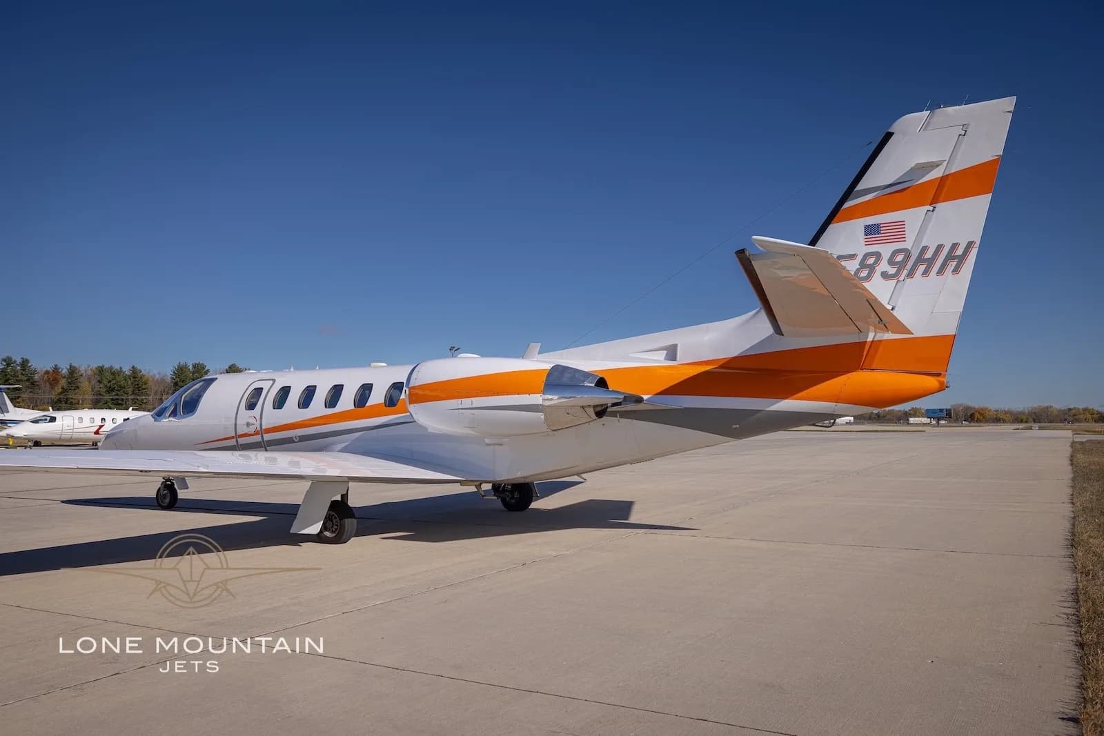 A rear quarter view of the white Cessna Citation Bravo business jet N589HH with orange and grey stripes on the tarmac.
