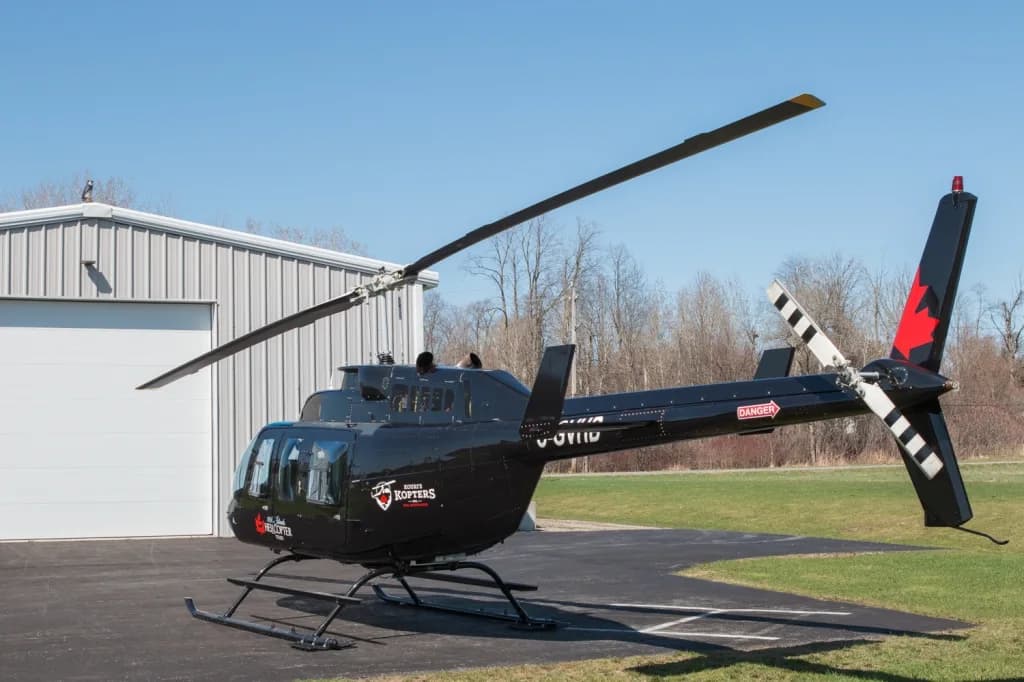 A black Bell 206 helicopter with registration C-GVHD is parked on a tarmac, showing its tail rotor with a red maple leaf design.