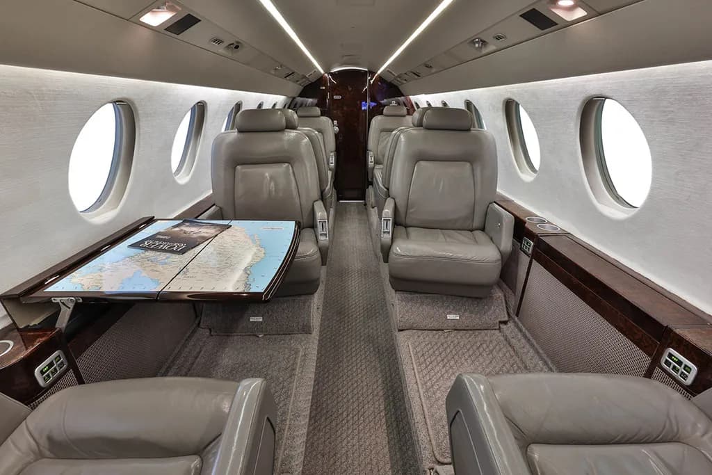 The luxurious interior cabin of a private jet with grey leather seats and a map on a table.