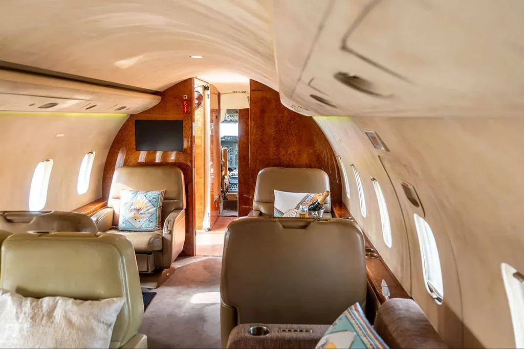 A private jet cabin interior looking forward, showing multiple seating areas and wood accents.