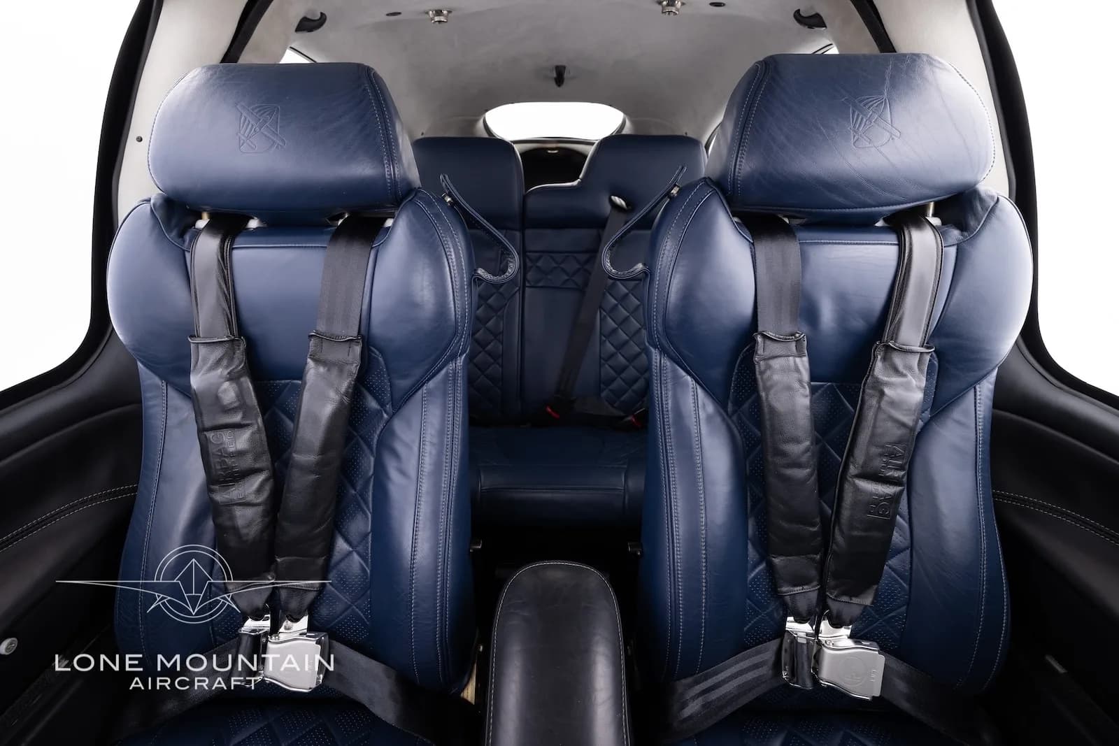 The dark blue quilted leather front seats of an aircraft cabin with seatbelts.