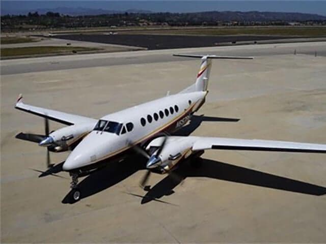 An aerial view of a white Beechcraft King Air B200 with gold and black stripes parked on an airfield.