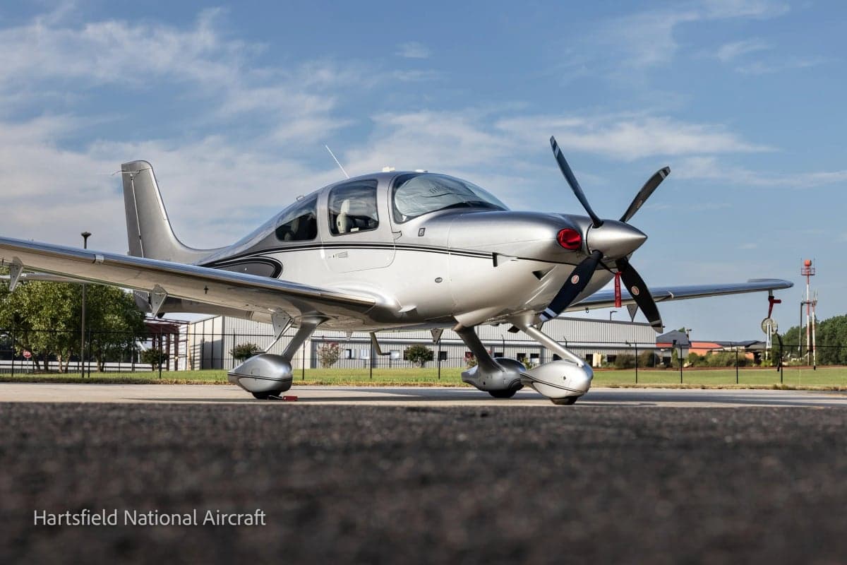 A Cirrus SR22T aircraft is parked on the tarmac with a silver paint scheme.