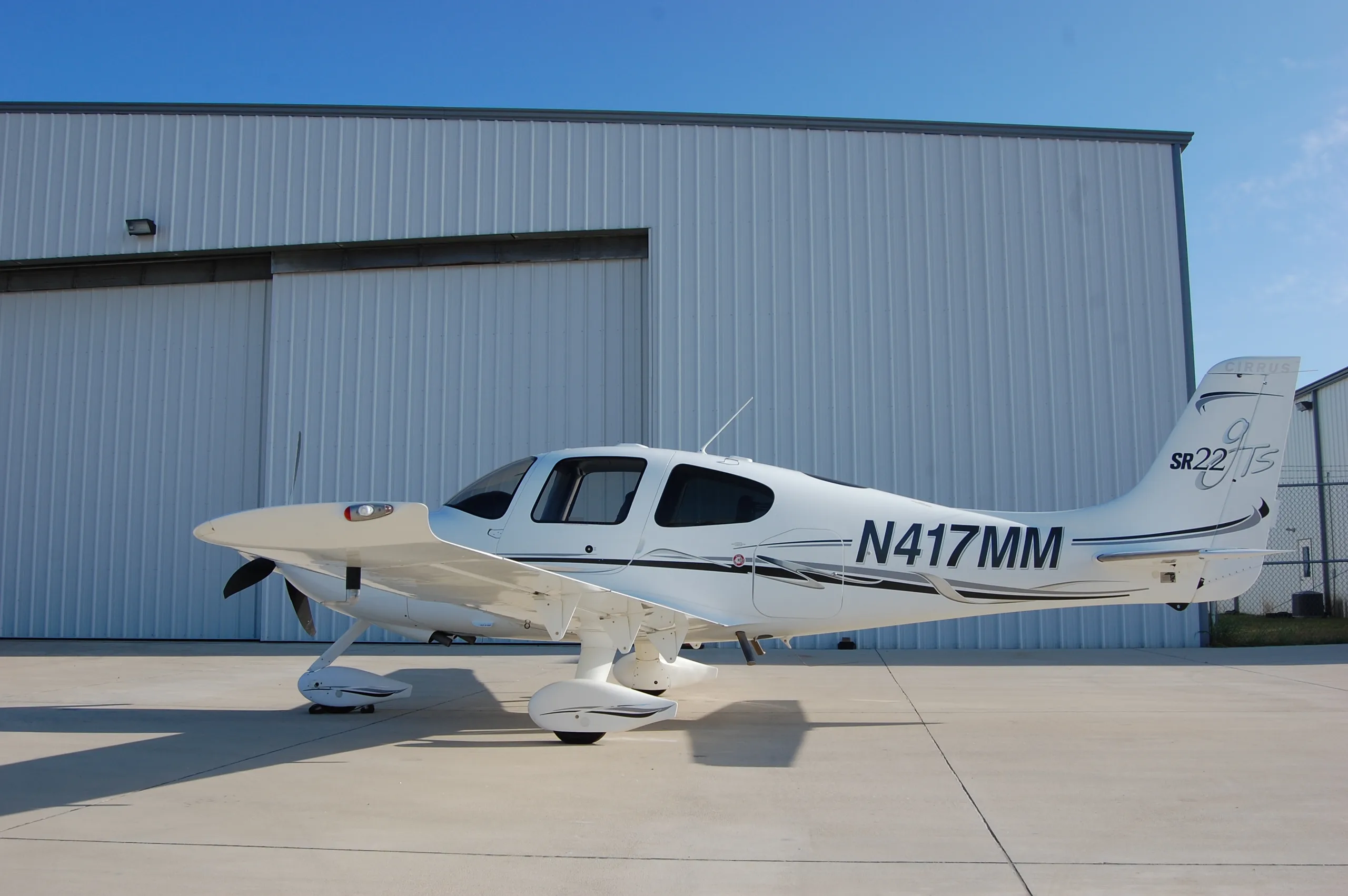 A side view of the white Cirrus SR22 aircraft, N417MM, parked in front of a hangar.