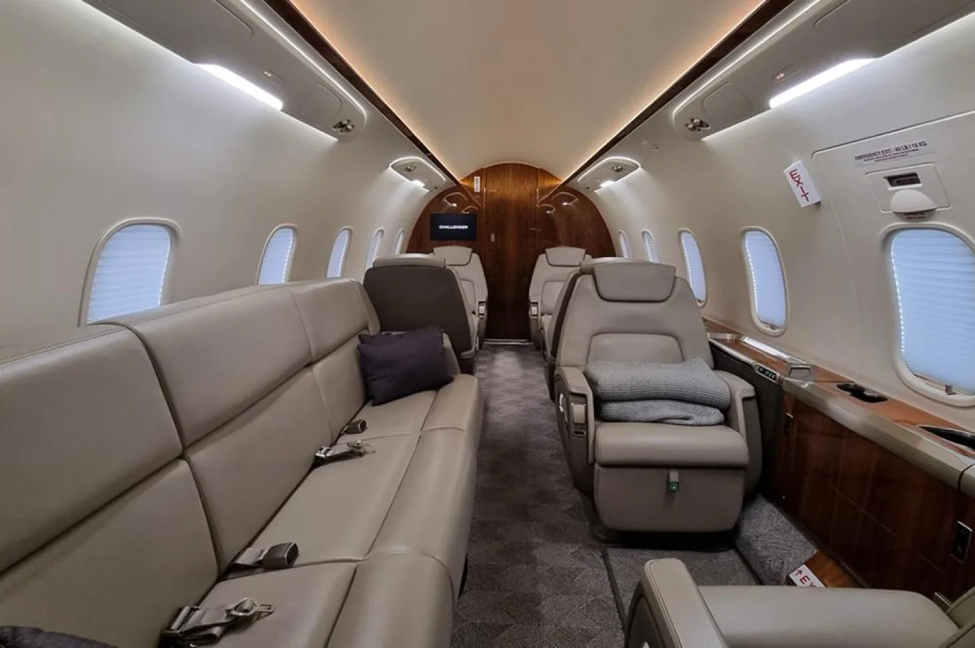 A view of the business jet's cabin interior features a long beige leather sofa on the left and individual club seats on the right, with wood accents and window shades.