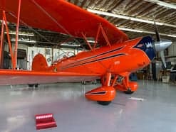 An orange biplane flying in the sky.