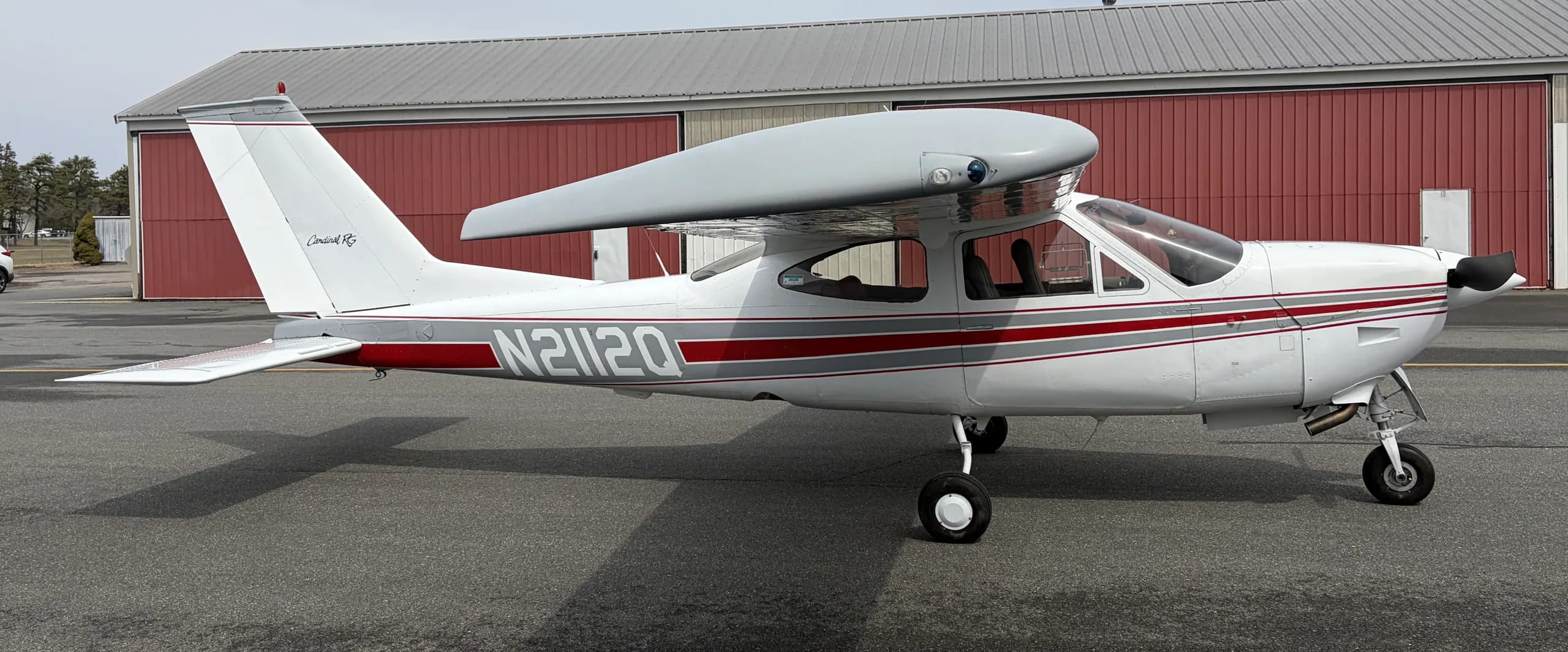 A side view of a white Cessna Cardinal RG with red and grey stripes, showing the N2112Q registration.