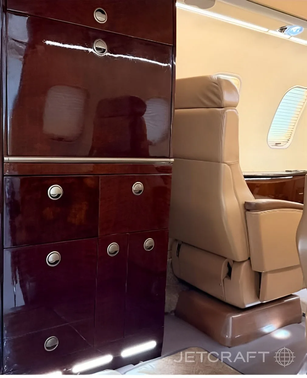 A polished dark wood cabinet next to a tan leather seat in the aircraft cabin.
