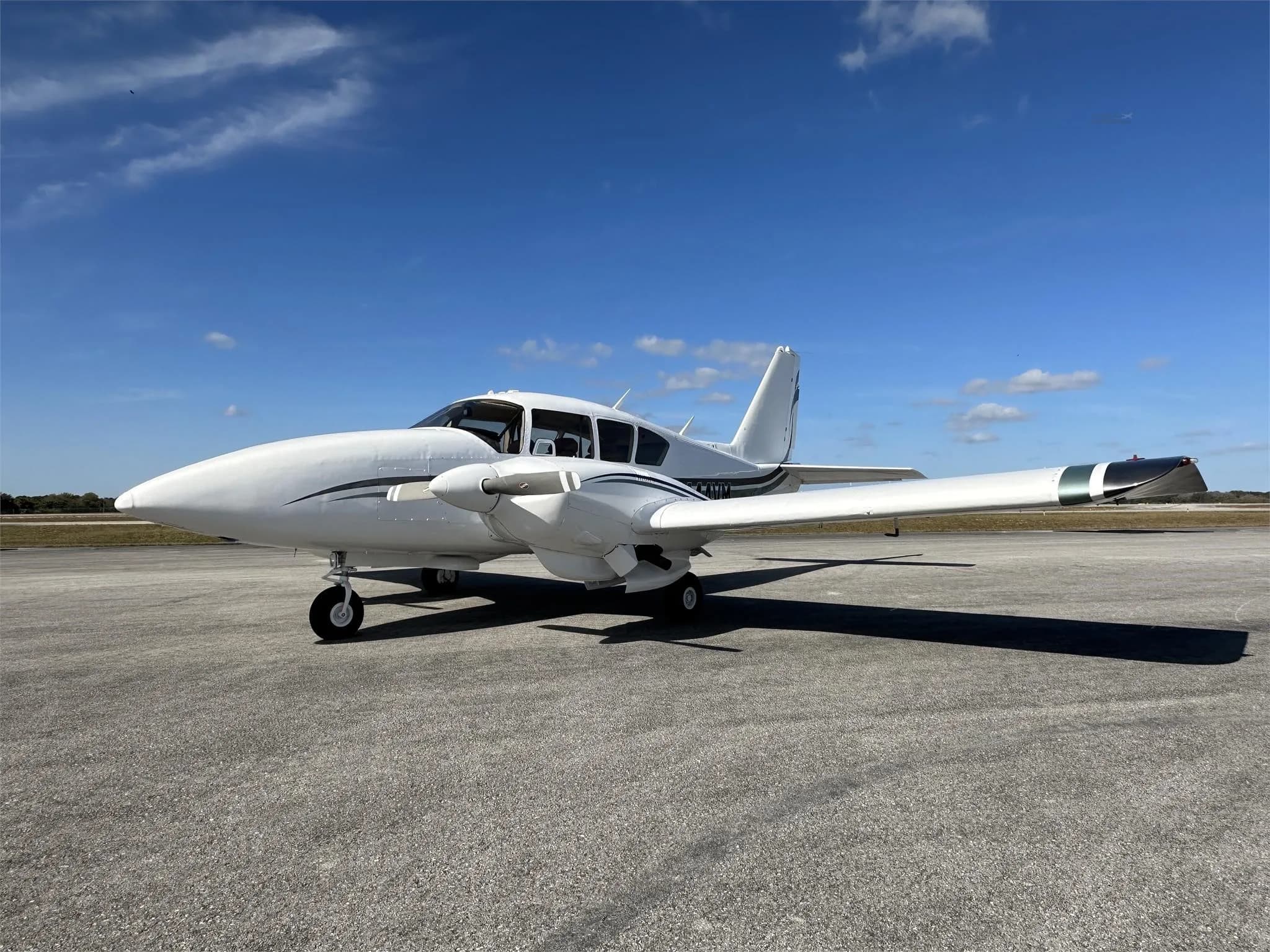 A front-side view of a white Piper aircraft with green and black stripes, registration N444VM, parked on an airfield.