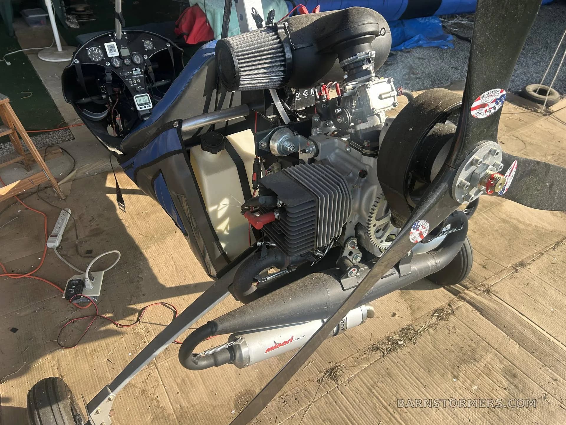 The exposed engine and propeller of a black ultralight autogyro, showing the air filter and exhaust.
