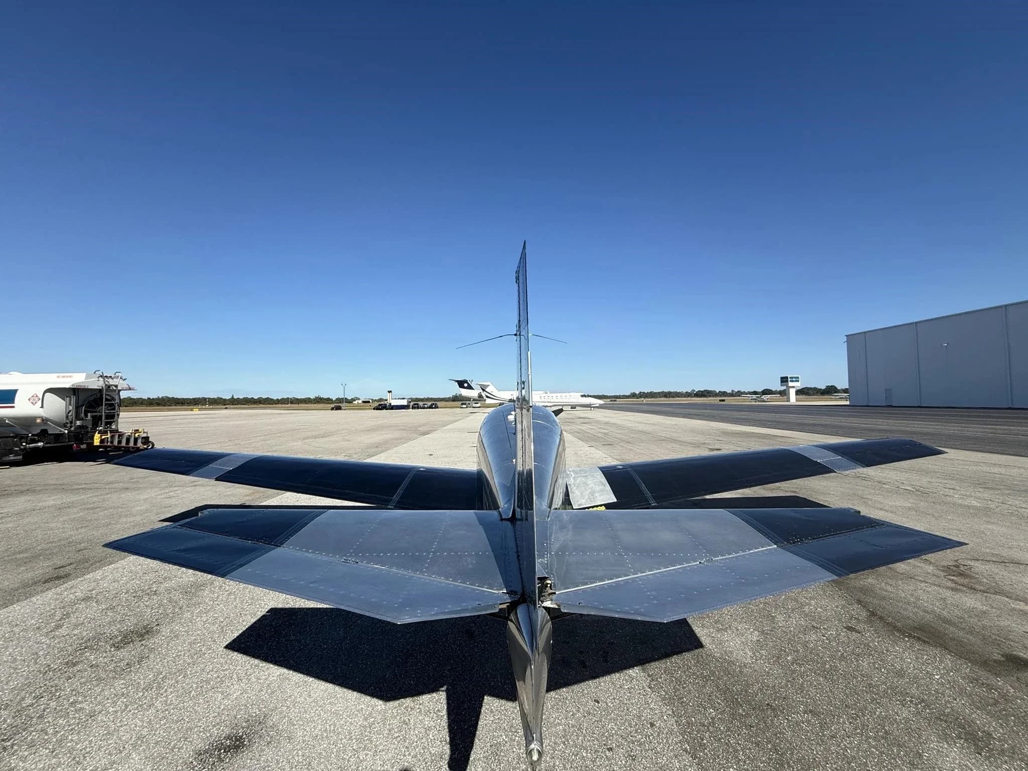 Rear view of a black and silver Mooney M20 aircraft, N5758Q, parked on an airfield with other aircraft in the distance.