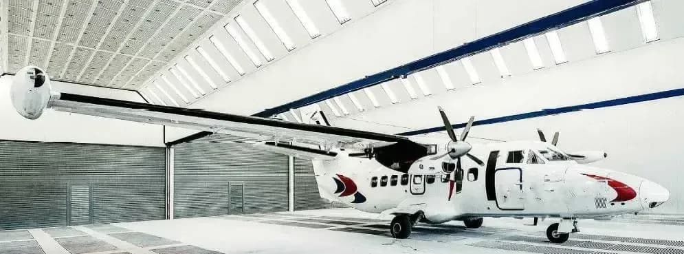 A white Let L-410 Turbolet aircraft is parked inside a hangar with its door open.