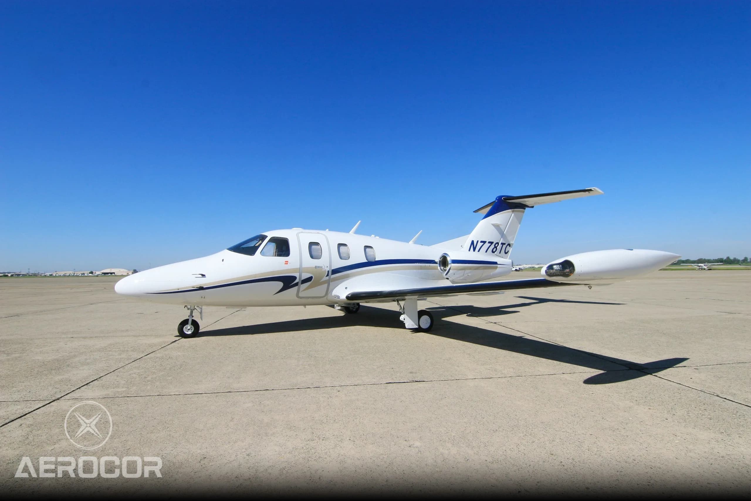 A white Eclipse 500 jet with blue and gold stripes on the tarmac under a clear blue sky.