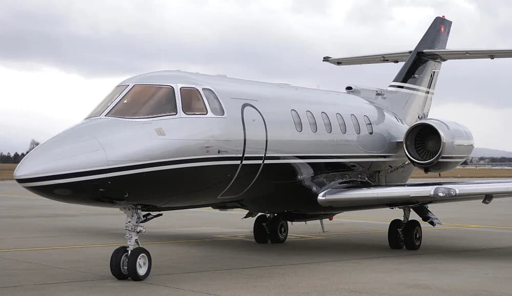 A front-side view of a silver and black Hawker 800XP business jet on an airfield.