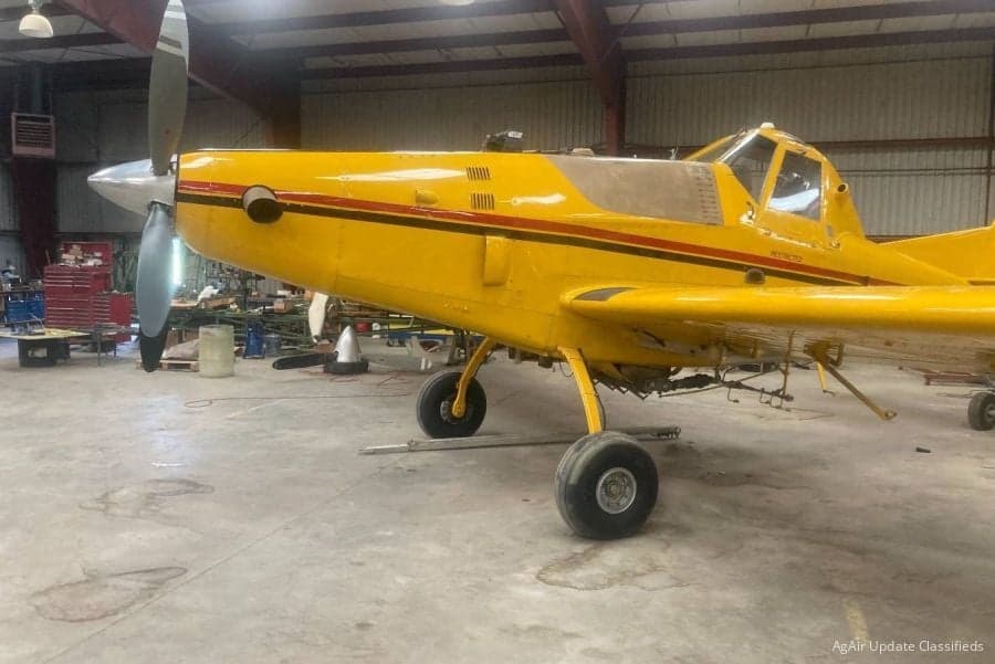 A yellow agricultural aircraft is parked inside a hangar.