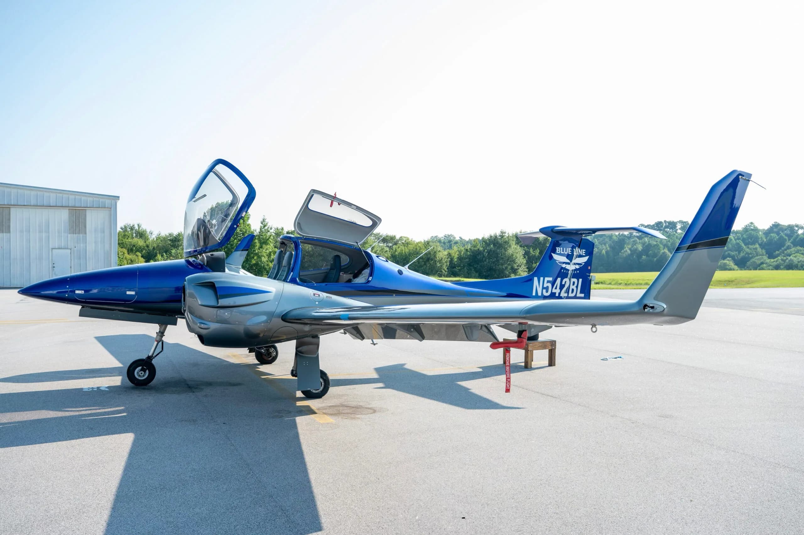Side view of a blue and grey Diamond DA42 aircraft with doors open, parked on an airfield.