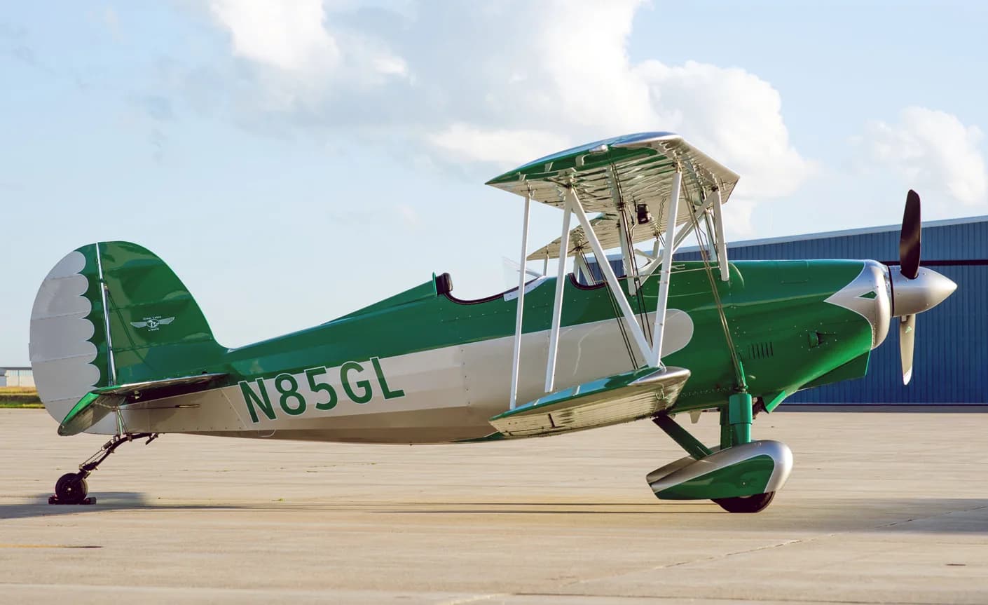 The N85GL biplane is parked on the tarmac with a hangar in the background.