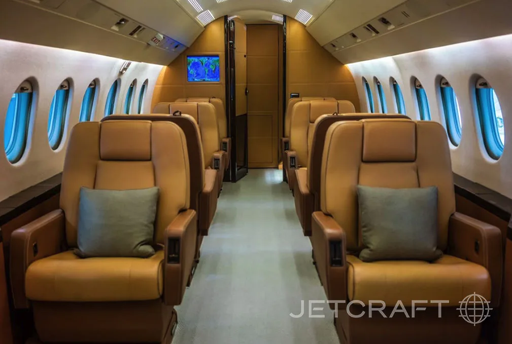 The luxurious interior of a business jet cabin with tan leather seats and grey pillows.