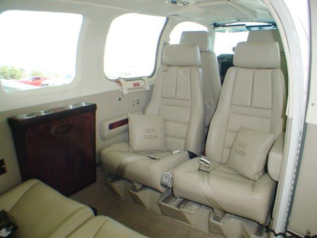 The tan leather interior of a Beechcraft Baron 58TC cabin shows two rows of seats and a side console.