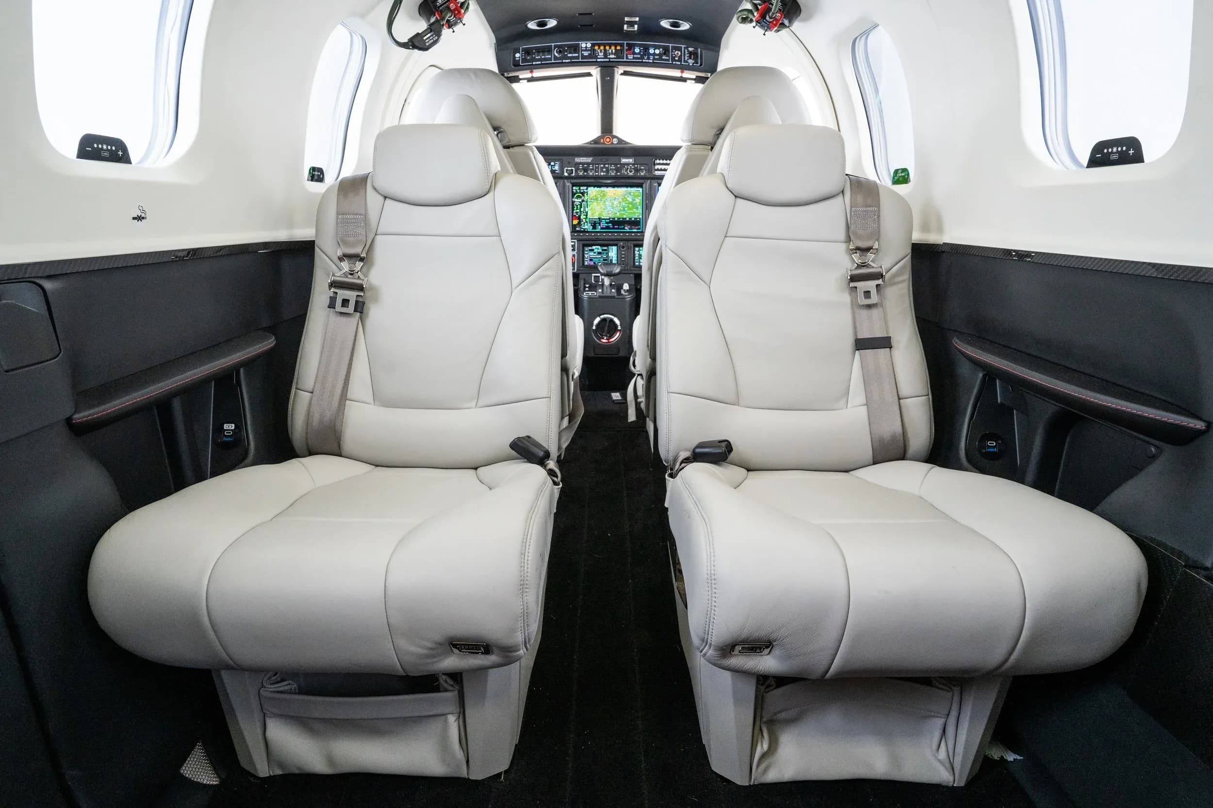 The aircraft cabin interior with two light-colored leather seats facing the rear, and the cockpit visible in the background.