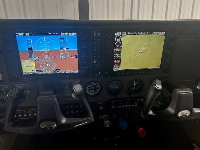The cockpit of an aircraft, showing two yokes and two large glass panel displays with flight and navigation data.