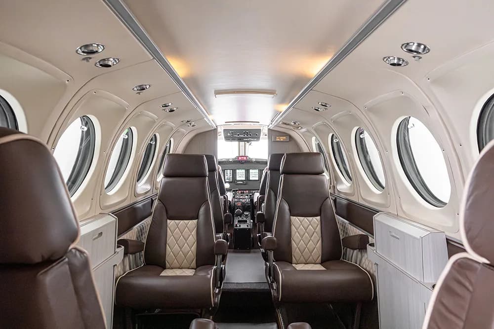 A view down the aircraft cabin aisle, showing brown and beige quilted seats and the cockpit in the distance.