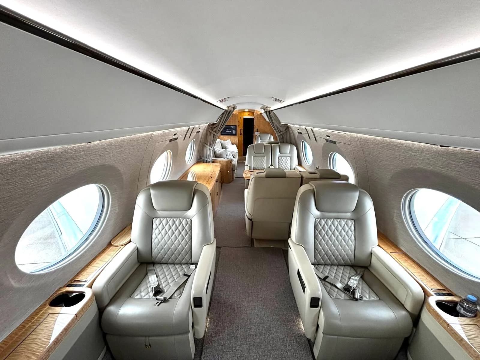 A wide-angle view of a luxurious private jet cabin with light-colored quilted leather seats and wooden accents.