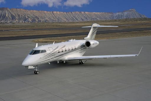 A Challenger 300 aircraft on the tarmac with mountains in the background.