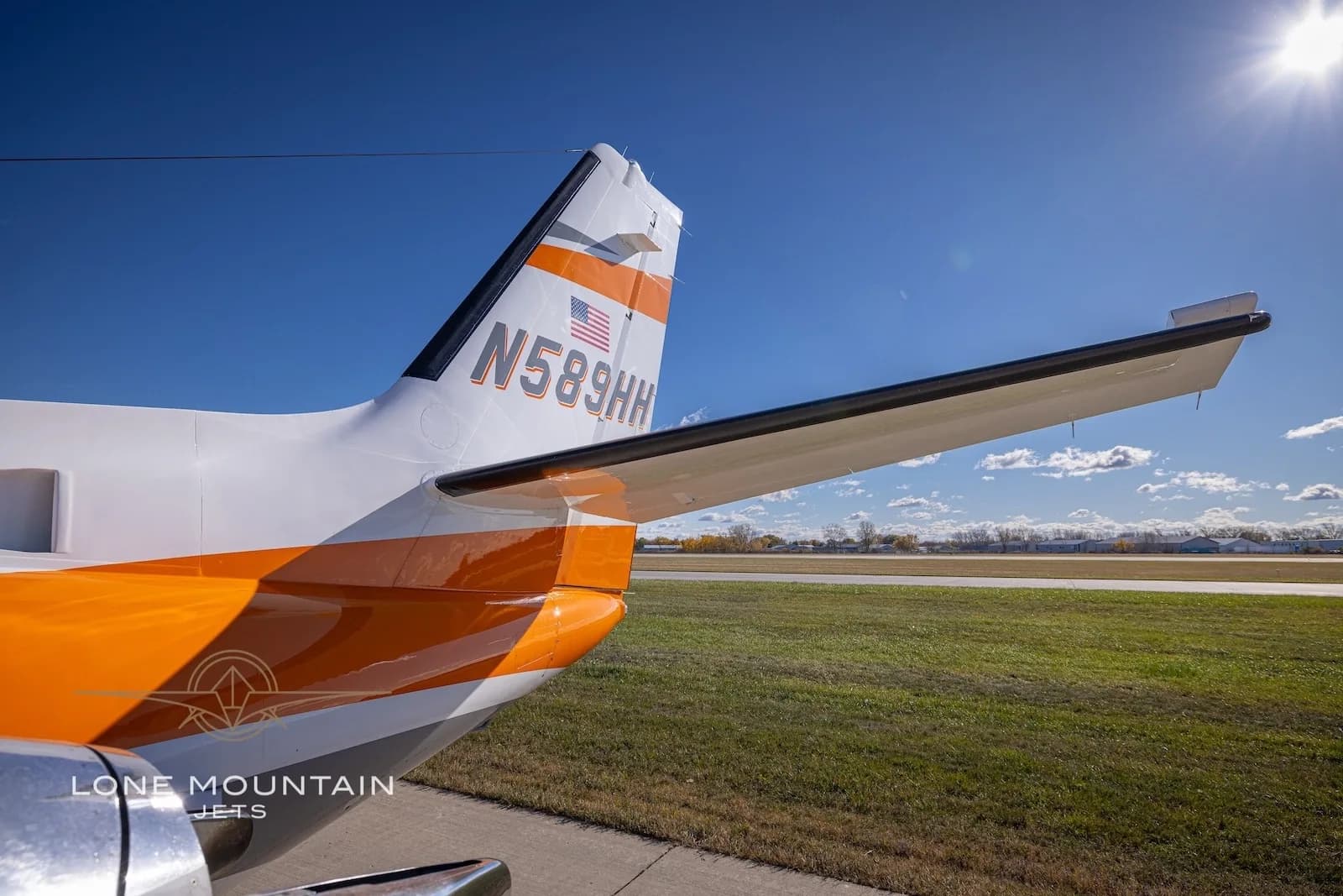 A close-up view of the tail of the Cessna Citation Bravo N589HH, showing the orange and grey stripe and US flag.