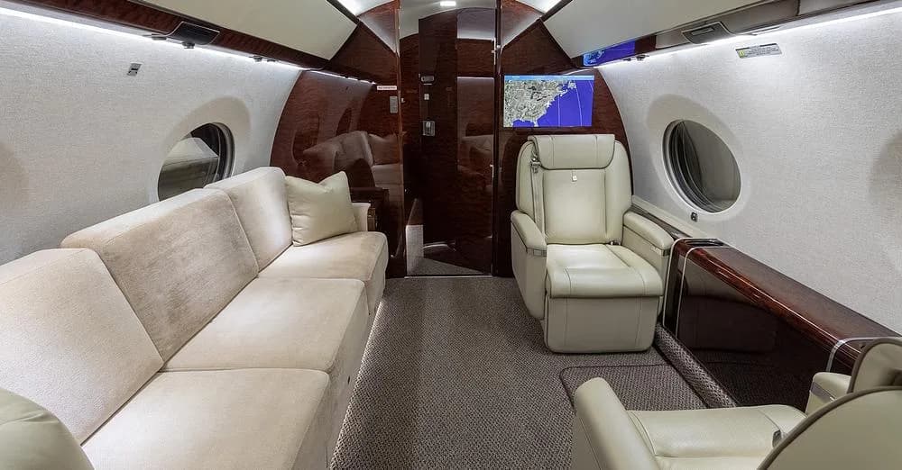 The Gulfstream G650 cabin interior featuring a long beige sofa and a single light leather seat with a map display.