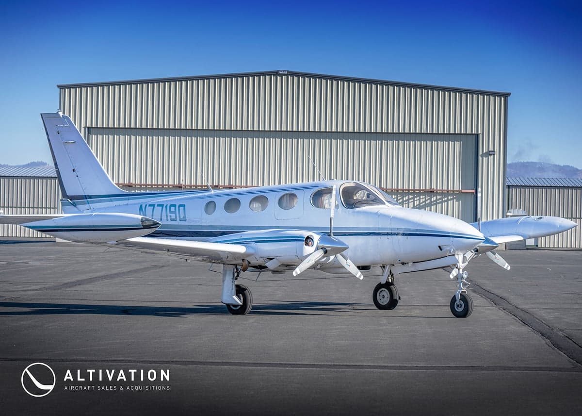 A white and blue twin-engine aircraft, registration N7719Q, sits on the tarmac.