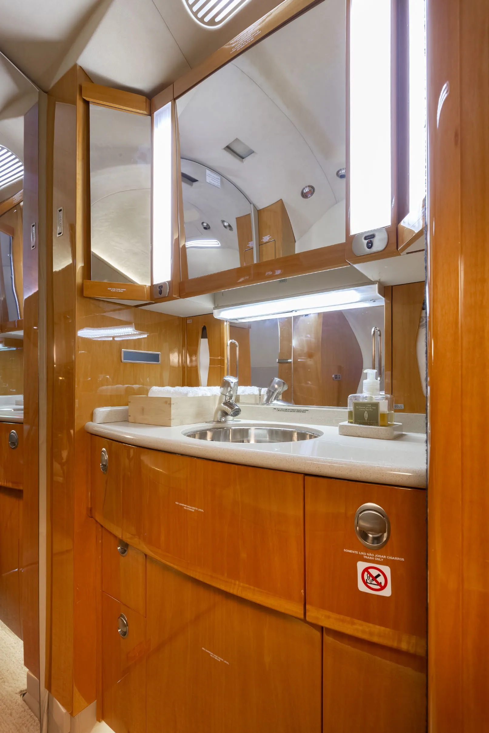The lavatory of a private jet, featuring a sink, large mirrors, and polished wooden cabinetry.