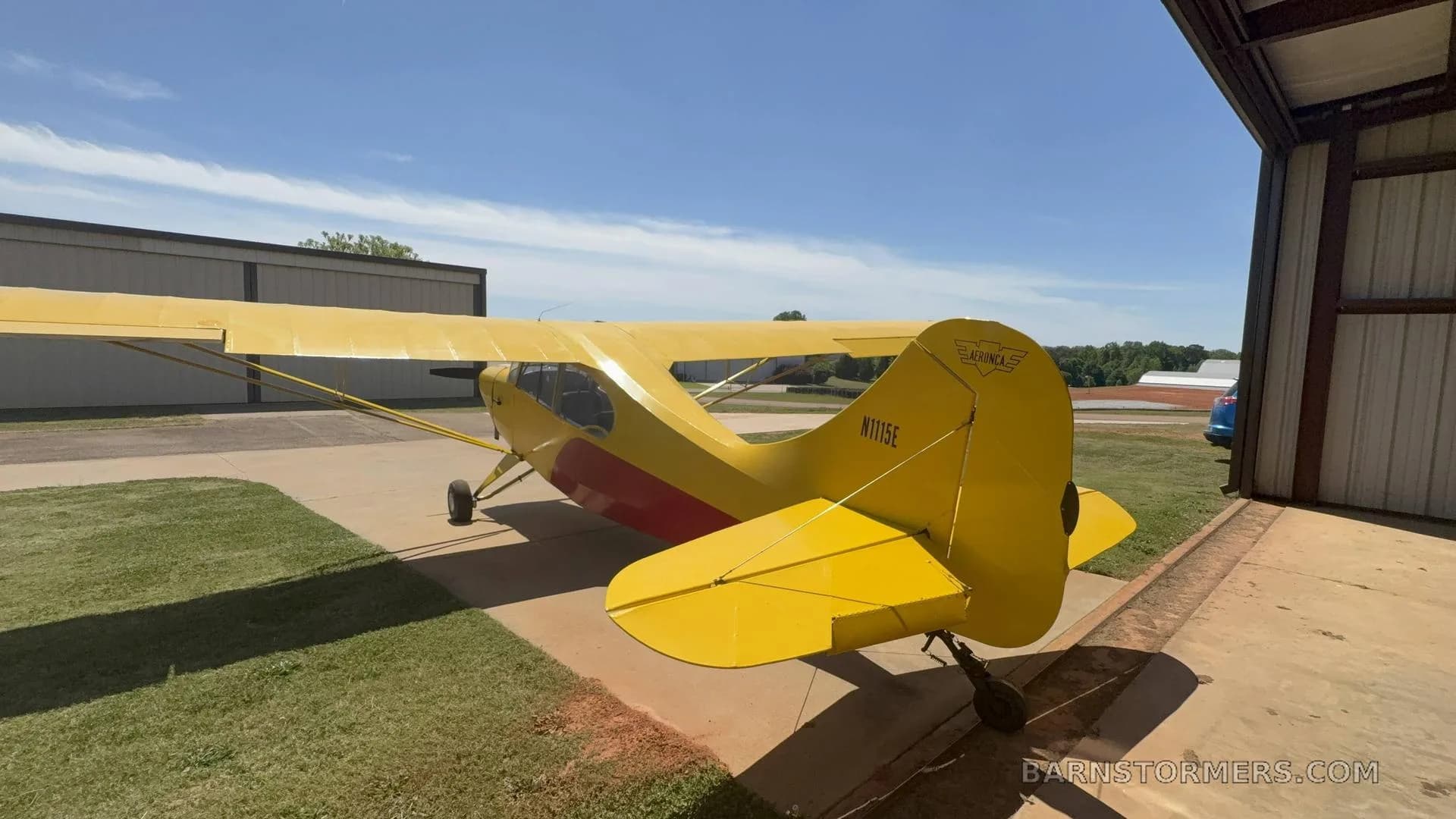 A rear view of the yellow single-engine aircraft, showing the tail number N115E, parked outside a hangar.