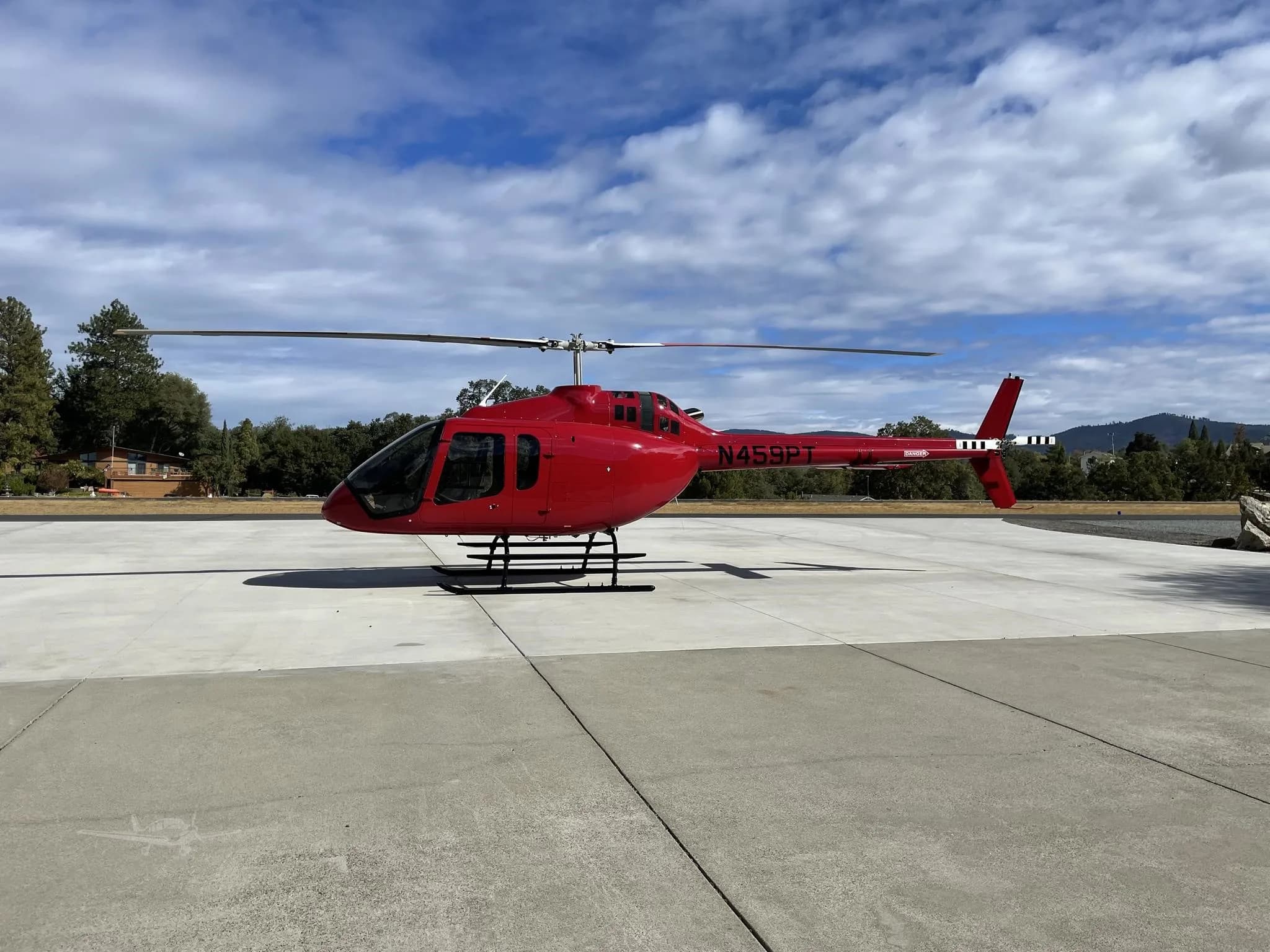 A red helicopter with tail number N459PT is parked on a concrete pad under a partly cloudy sky.