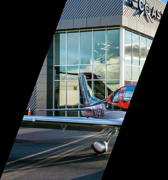 A red and silver single-engine aircraft, N155W, parked in front of a modern building.