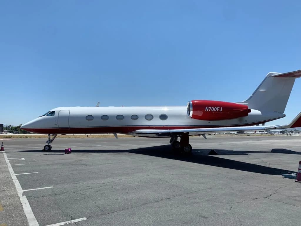 Side view of a Gulfstream jet with red accents parked on the tarmac.