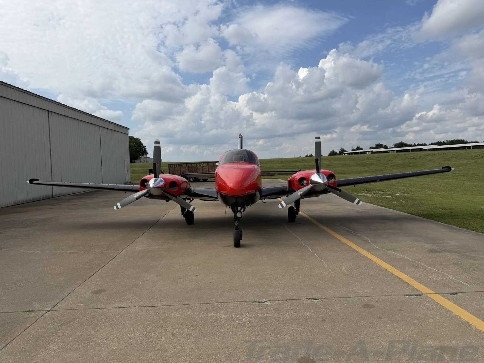 Front view of the red and black twin-engine propeller aircraft, N10NF, parked on an airfield tarmac.