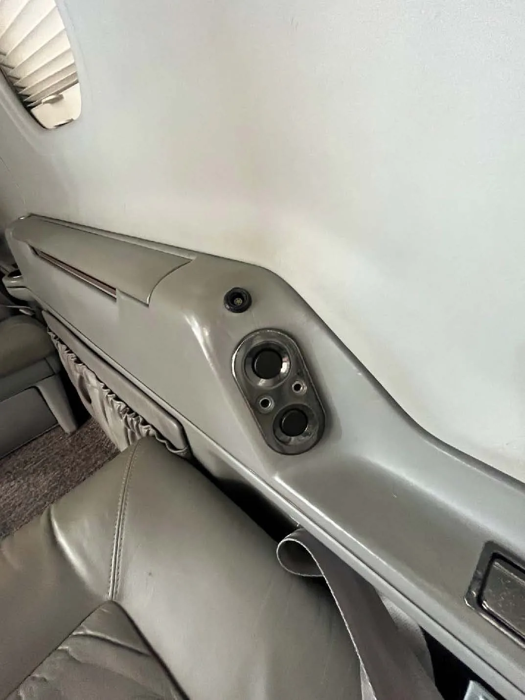 A close-up of a control panel on the side wall of the aircraft cabin next to a seat.