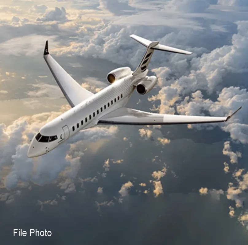 A white business jet with two rear-mounted engines flies through a cloudy sky.