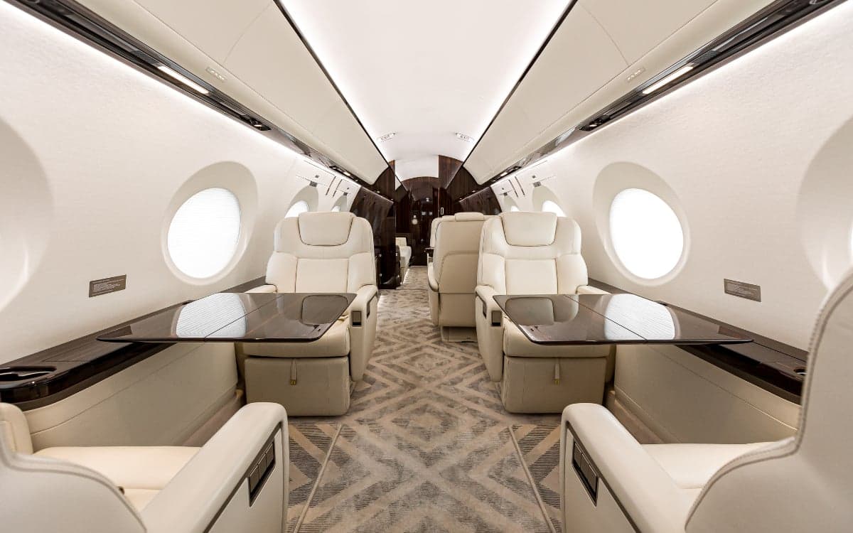 A view down the aisle of the Gulfstream G500 cabin featuring cream-colored leather seats and dark wood accents.