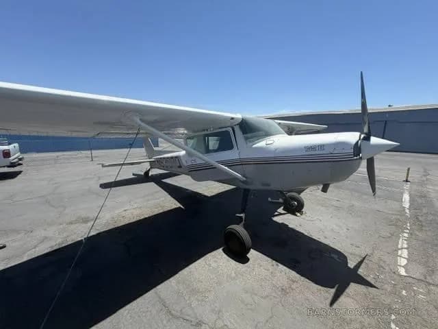 A white and grey single-engine propeller aircraft with a dark stripe on the fuselage, parked on an asphalt ramp under a clear blue sky.