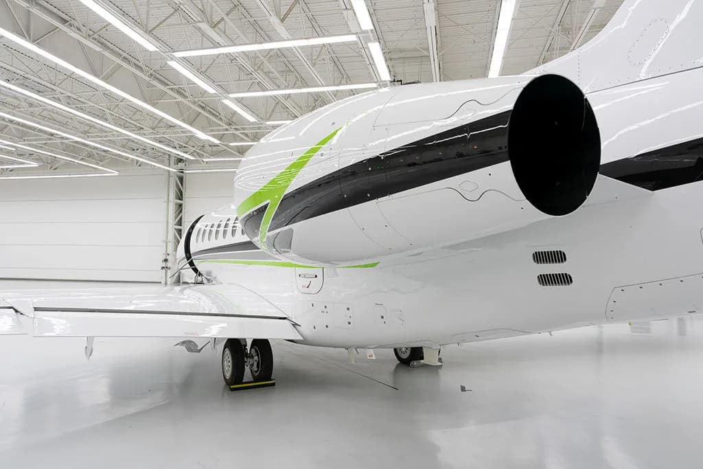 A close-up rear view of the engine and tail section of a white business jet with green and black stripes.