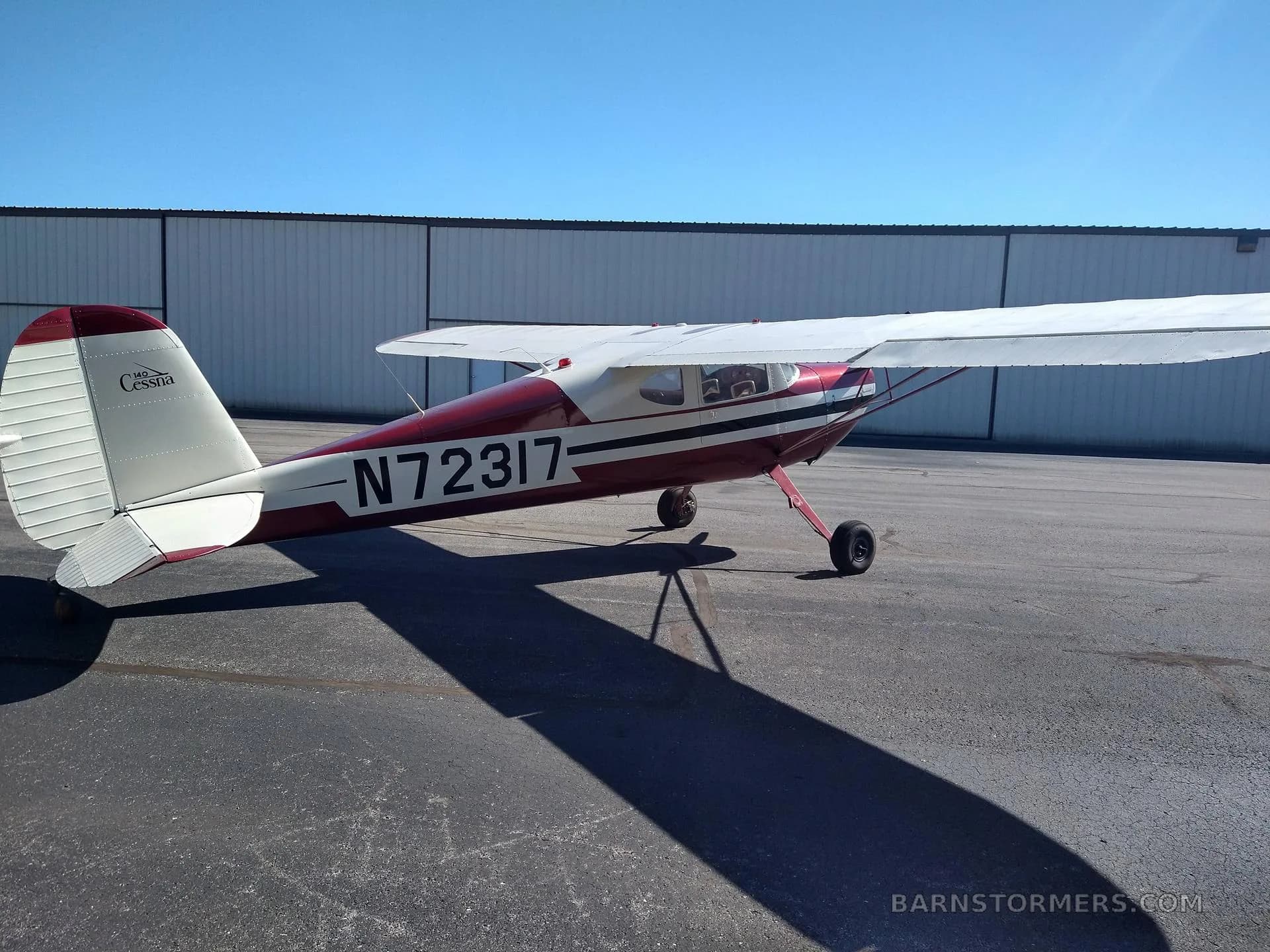 A rear-side view of a red and white Cessna 140 aircraft (N72317) with a conventional tail, parked on an asphalt tarmac.