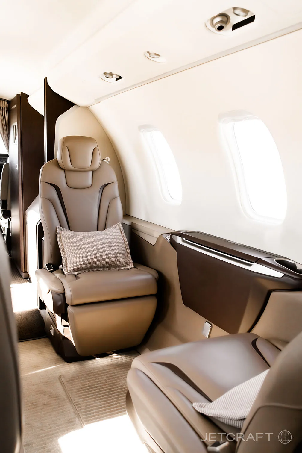 A side view of the aircraft cabin shows a single light brown leather seat next to a window, with another seat partially visible.