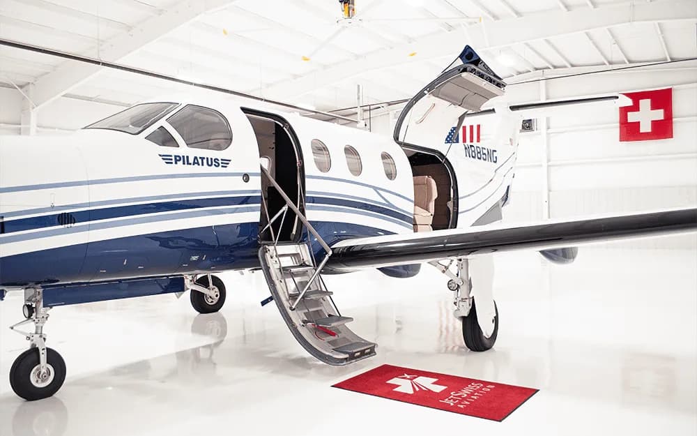 A white and blue Pilatus PC-12 aircraft with its main cabin door and cargo door open, showing the integrated airstair.