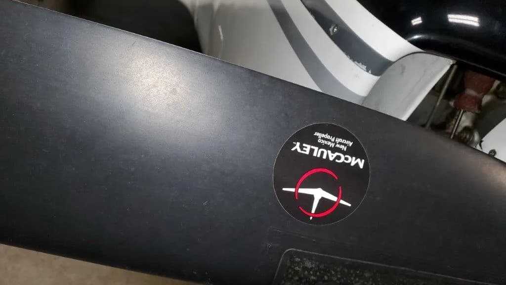 Close-up of a black aircraft propeller blade with a round McCauley sticker.
