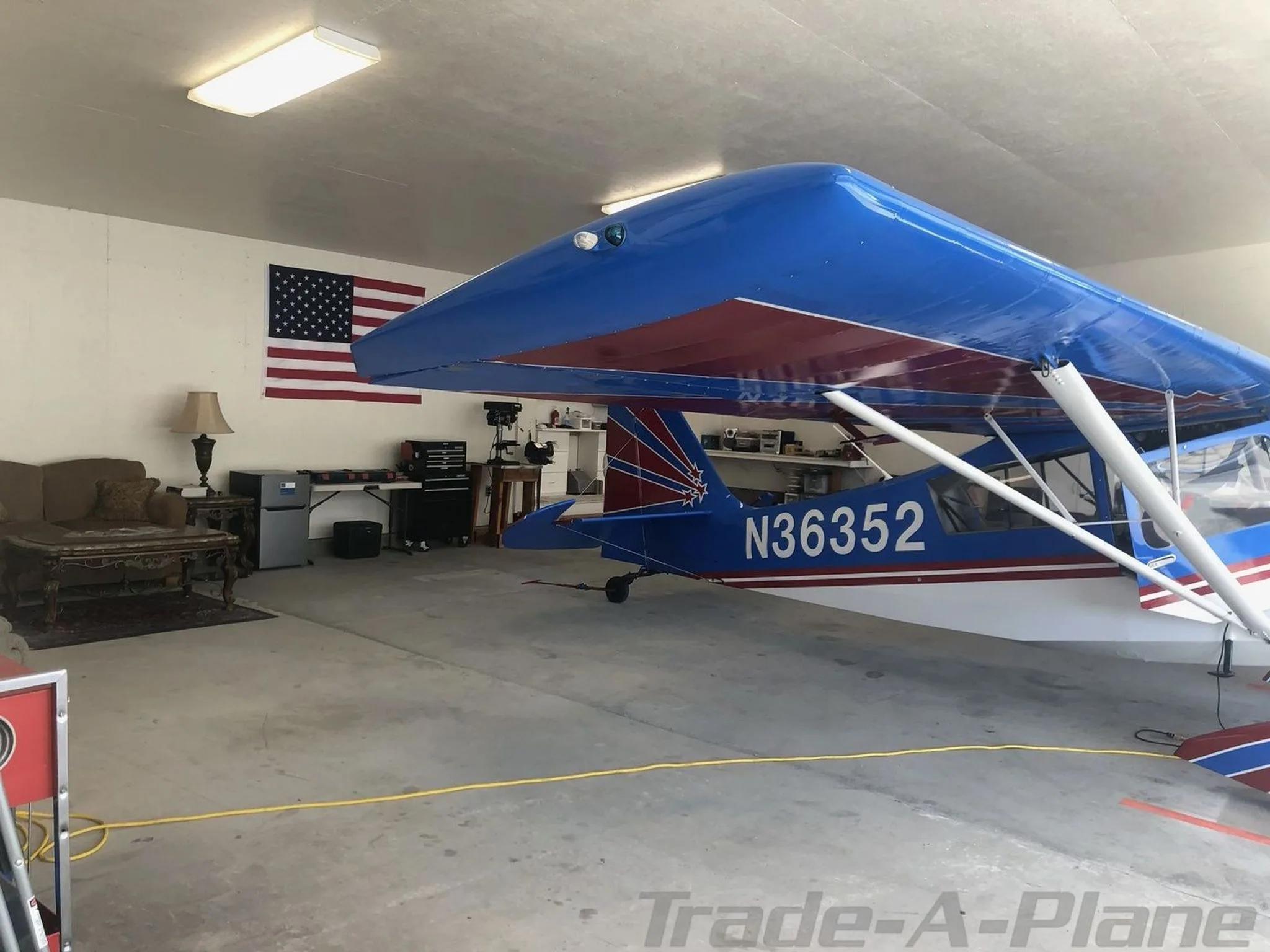 A blue and white high-wing aircraft, N36352, parked in a hangar with an American flag and lounge area.