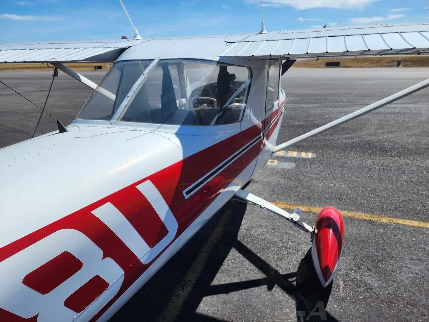 A close-up view of the front-right fuselage of a white and red Cessna 150 aircraft, showing part of the N-number.