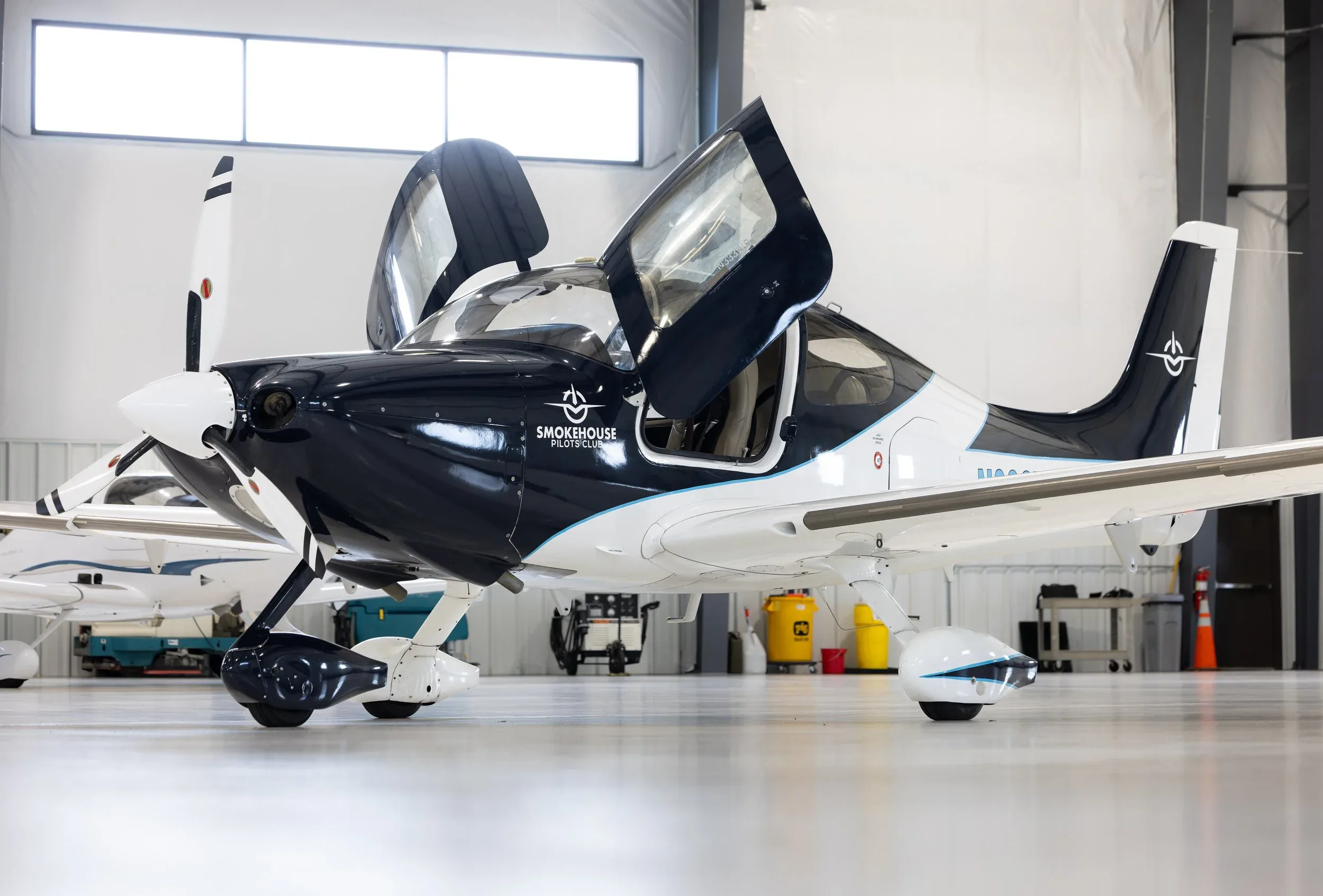 Front quarter view of a black and white Cirrus SR22T aircraft with its doors open inside a hangar.